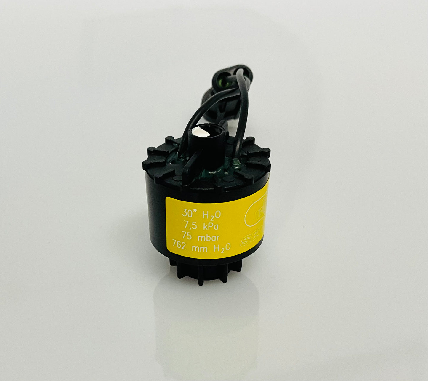 A black electrical indicator with a cable connection and yellow label, that reads '30" H2O', '7,5 kPa', '75 mbar', '762mm h20'. Shown on a reflective white surface.