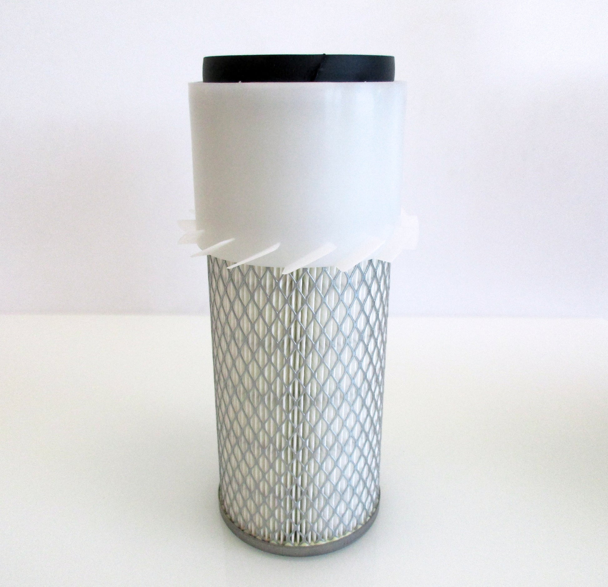 A cylindrical replacement air filter with a white plastic upper section with fins, a black seal top and a white pleated media surrounded by metal mesh, with grey base shown on a white background.