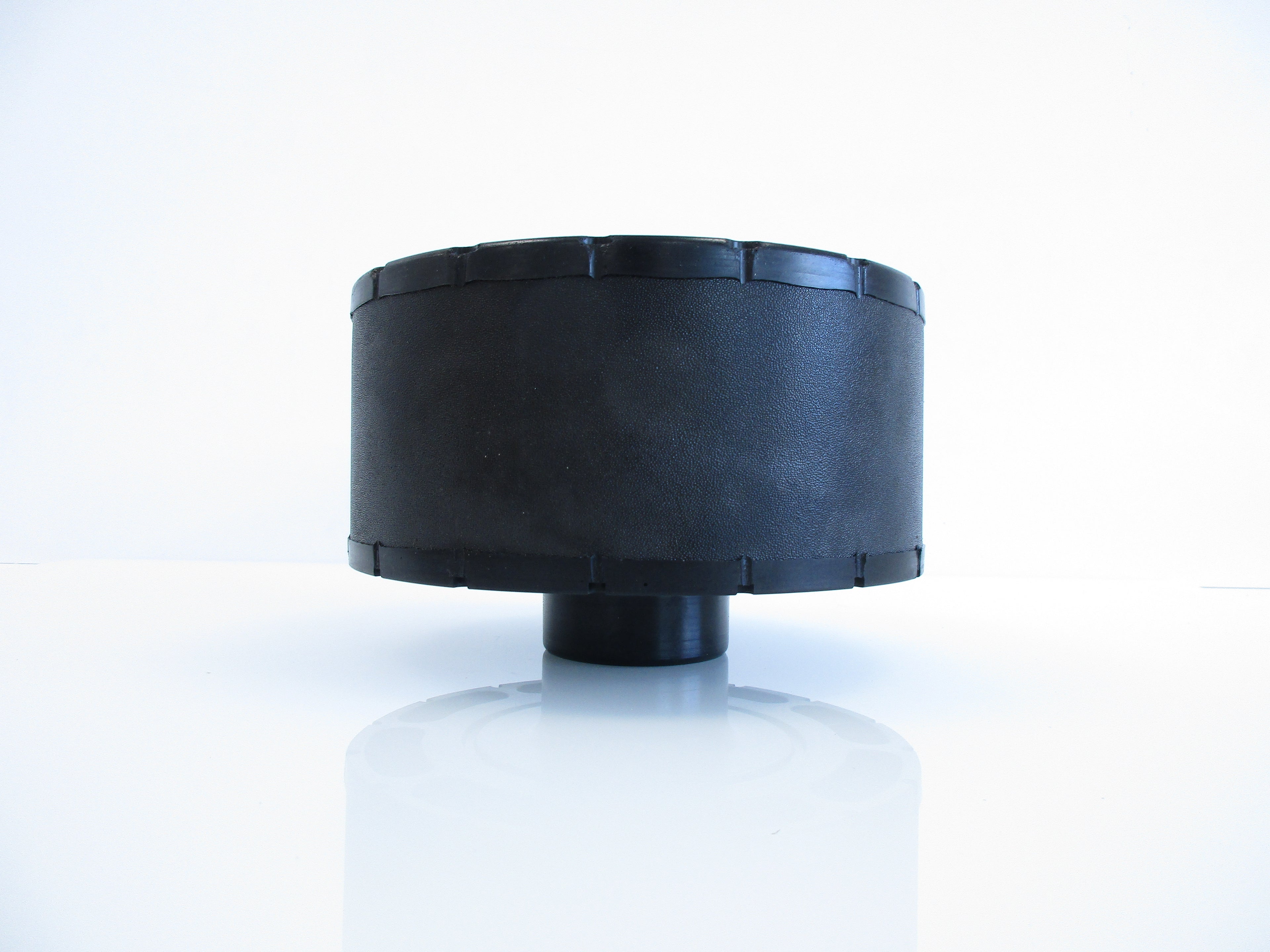 A black cylindrical plastic air cleaner with a stepped top rim, shown on a reflective white surface against a white background.