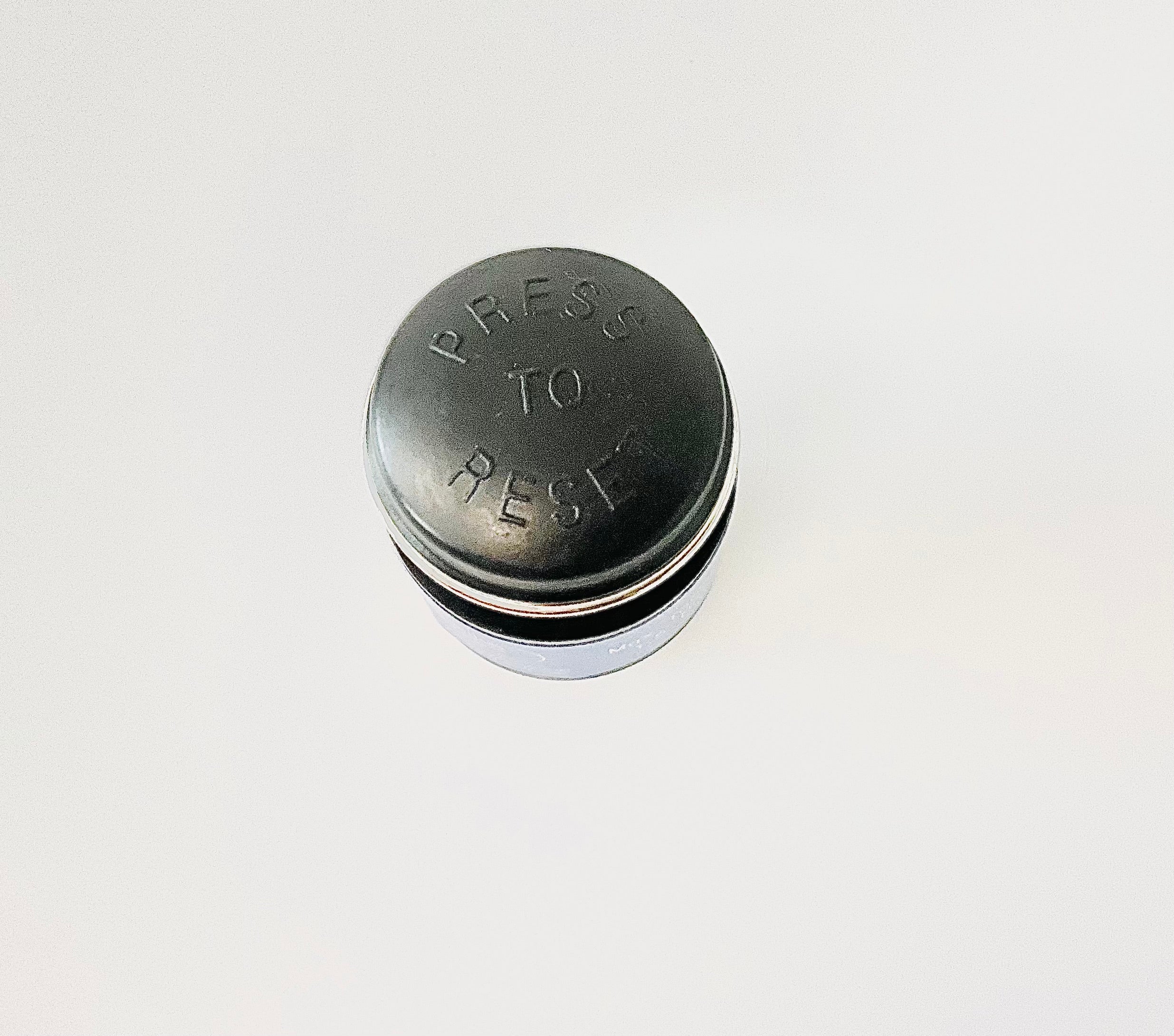 the top of a cylindrical indicator, showing the embossed text 'PRESS TO REST' on the top surface, set against a plain white background.