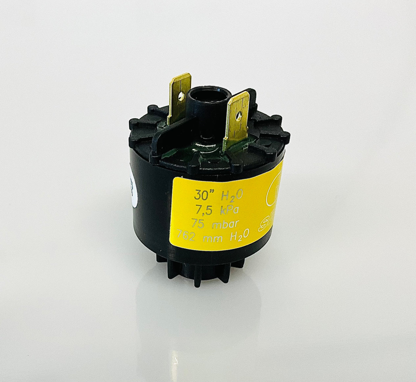 A small black cylindrical electrical indicator with two metal pins at the top, and a yellow label reading '30 H2O', 7,5 kPa', '75 mbar' and '762 mm H2O', shown on a reflective white surface.