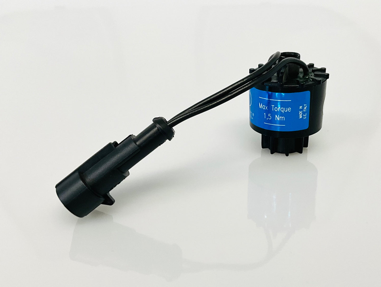A black electrical indicator with a cable connection and blue label, that reads 'Max Torque 1,5 Nm', 'MADE IN U.E ITALY',  shown on a reflective white surface.