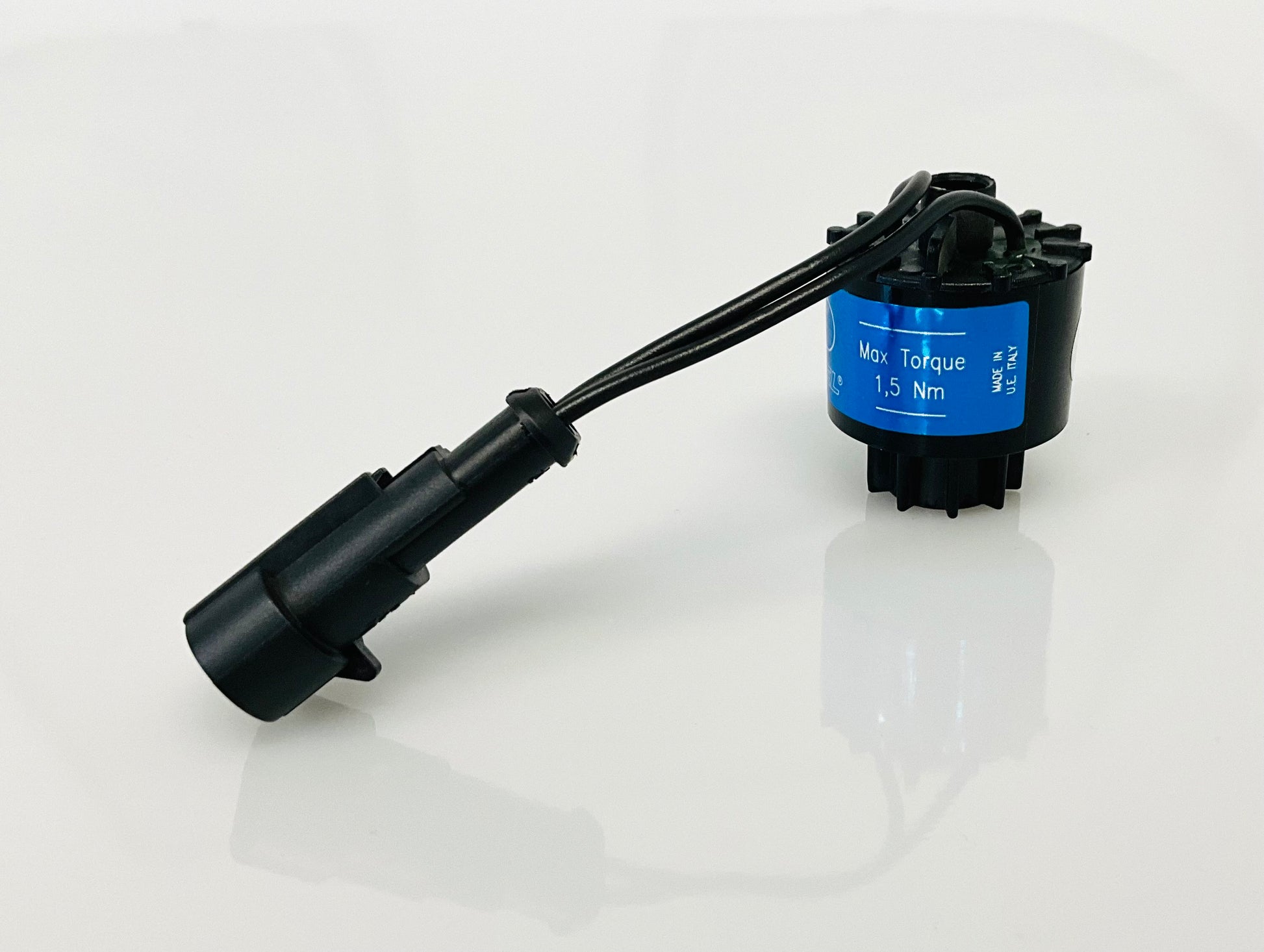 A black electrical indicator with a cable connection and blue label, that reads 'Max Torque 1,5 Nm', 'MADE IN U.E ITALY',  shown on a reflective white surface.
