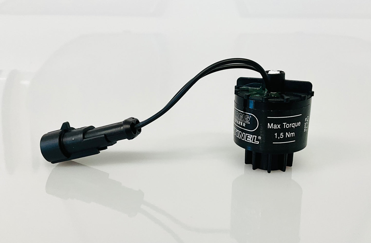 A black electrical indicator with a cable connection and a label, that reads 'Max Torque 1,5 Nm', shown on a reflective white surface.
