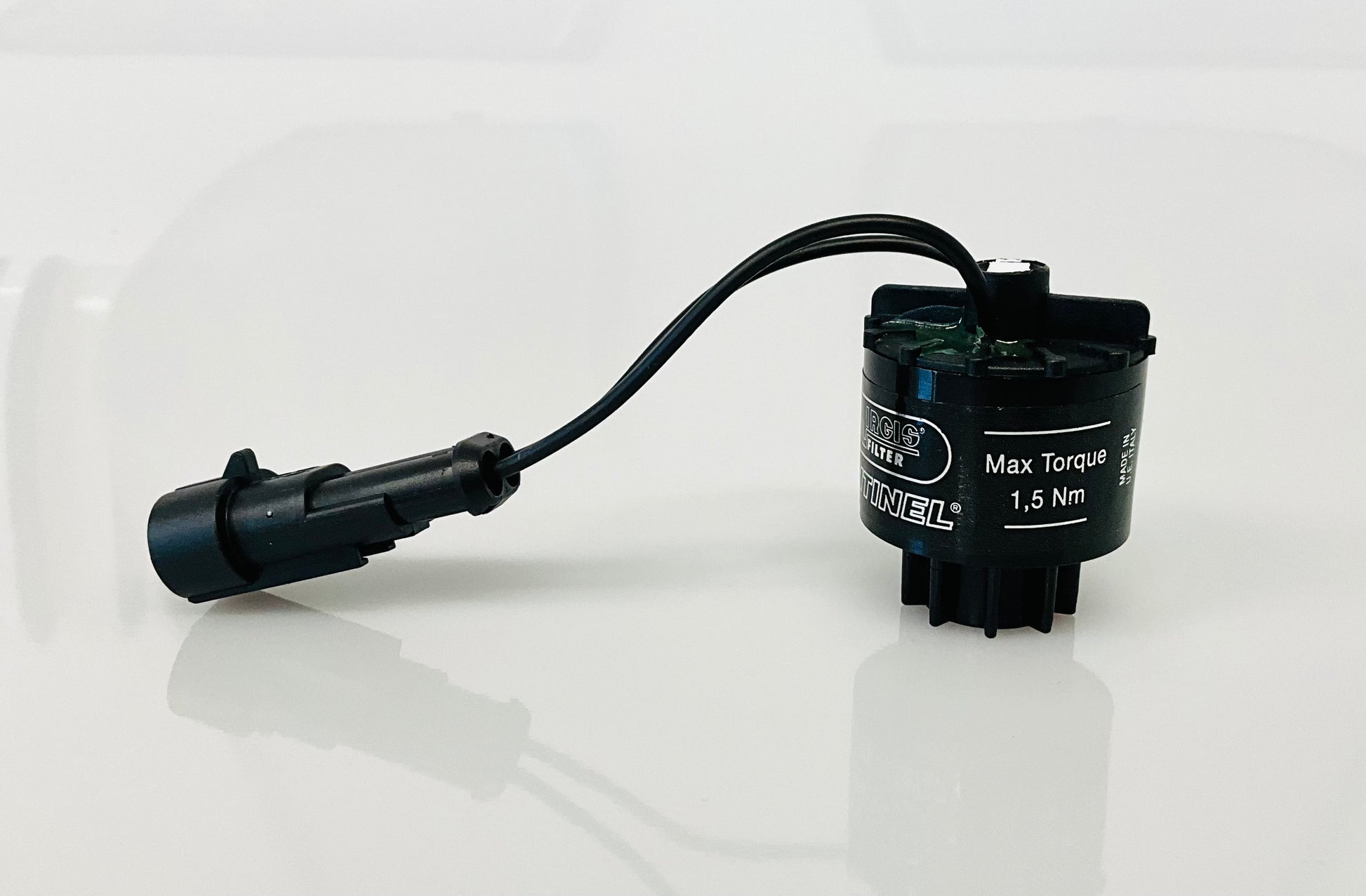 A black electrical indicator with a cable connection and a label, that reads 'Max Torque 1,5 Nm', shown on a reflective white surface.