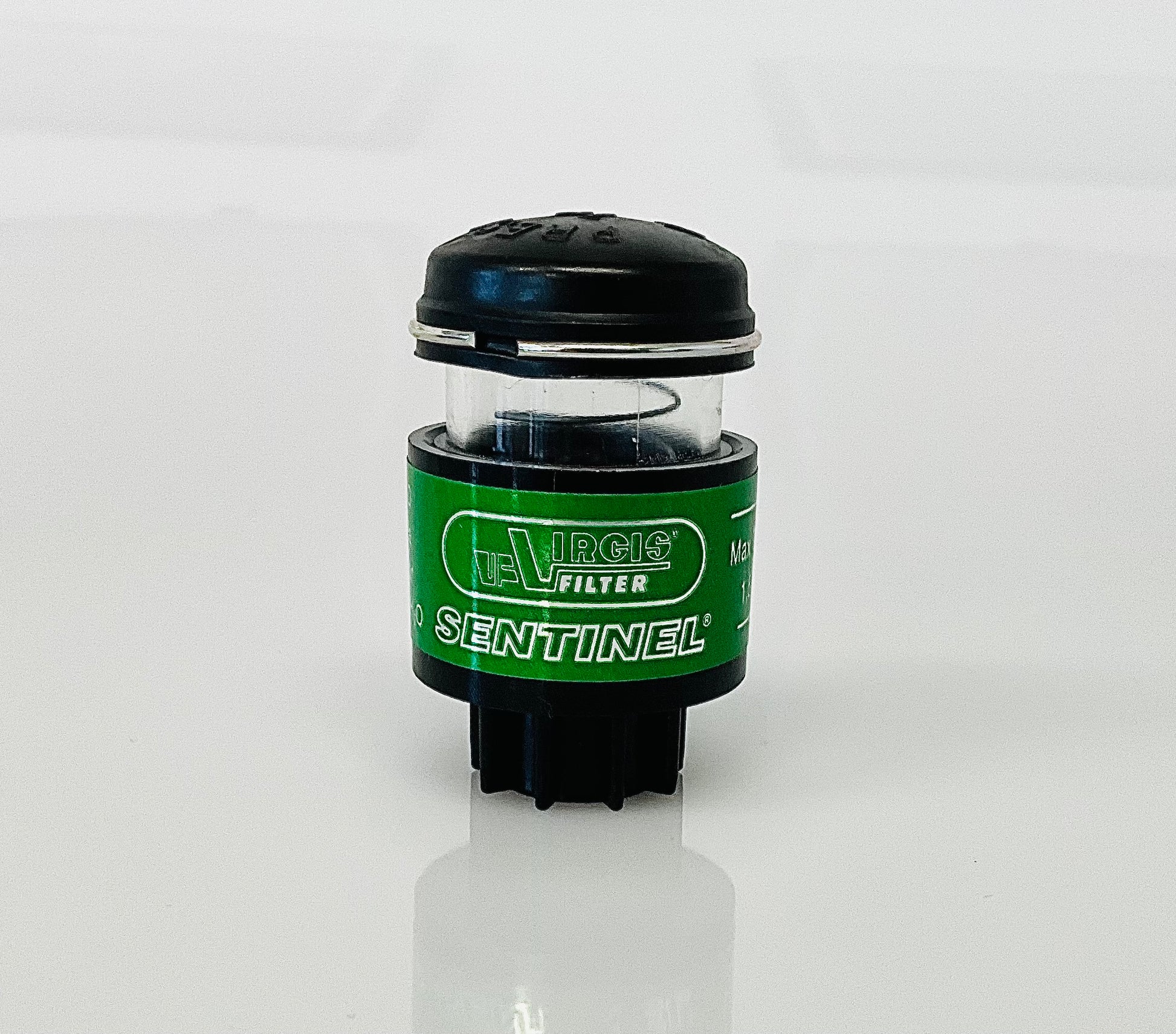 A small black cylindrical optical indicator with press button top, with a green label labelled 'Virgis Filter' and 'Sentinel', shown on a reflective white surface.