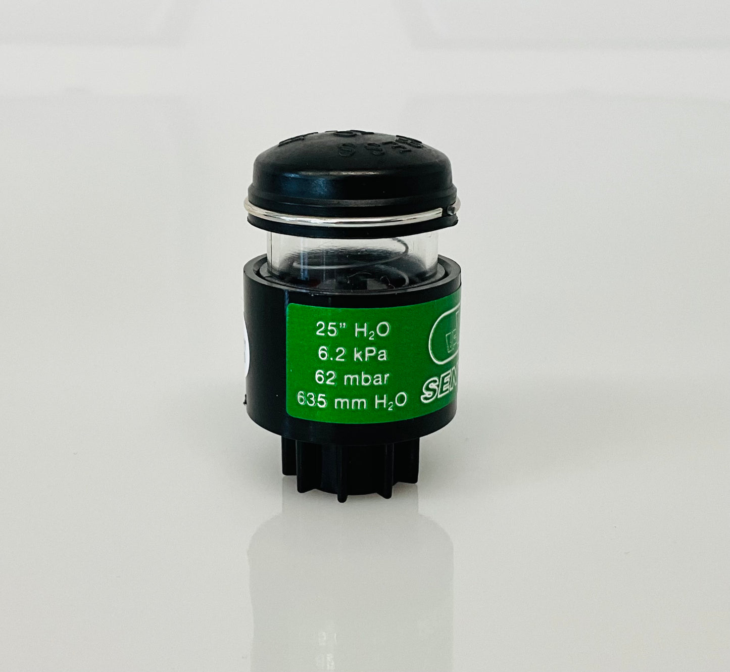 A small black cylindrical optical indicator with press button top, with a green label reading '25" H2O 6.2 kPa 62 mbar 635 mm H2O', photographed on a white background.
