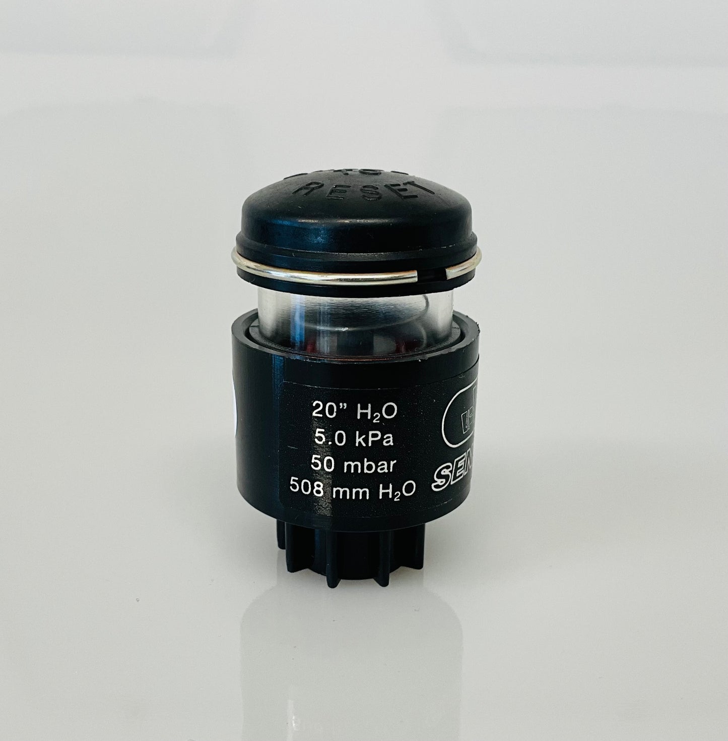 A small black cylindrical optical indicator with press button top, with white printed specifications ('20" H2O', '5.0 kPa', '50 mbar', '508 mm H2O') on a clean white background.