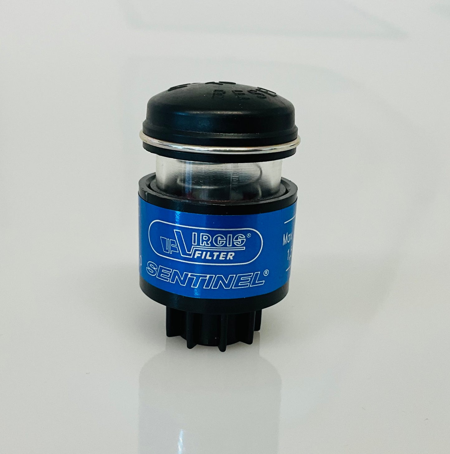 A small black cylindrical optical indicator with press button top, with a blue label labelled 'Virgis Filter' and 'Sentinel', shown on a reflective white surface.