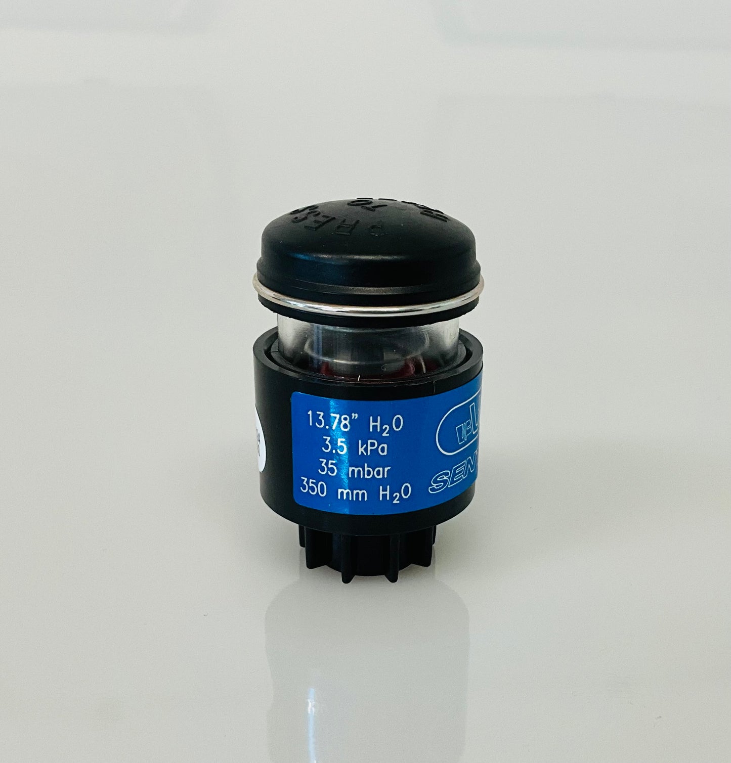 A small black cylindrical optical indicator with press button top, with a blue label reading '13.78" H2O, '3.5 kPa', '35 mbar', '350 mm H2O', photographed on a clean white background.