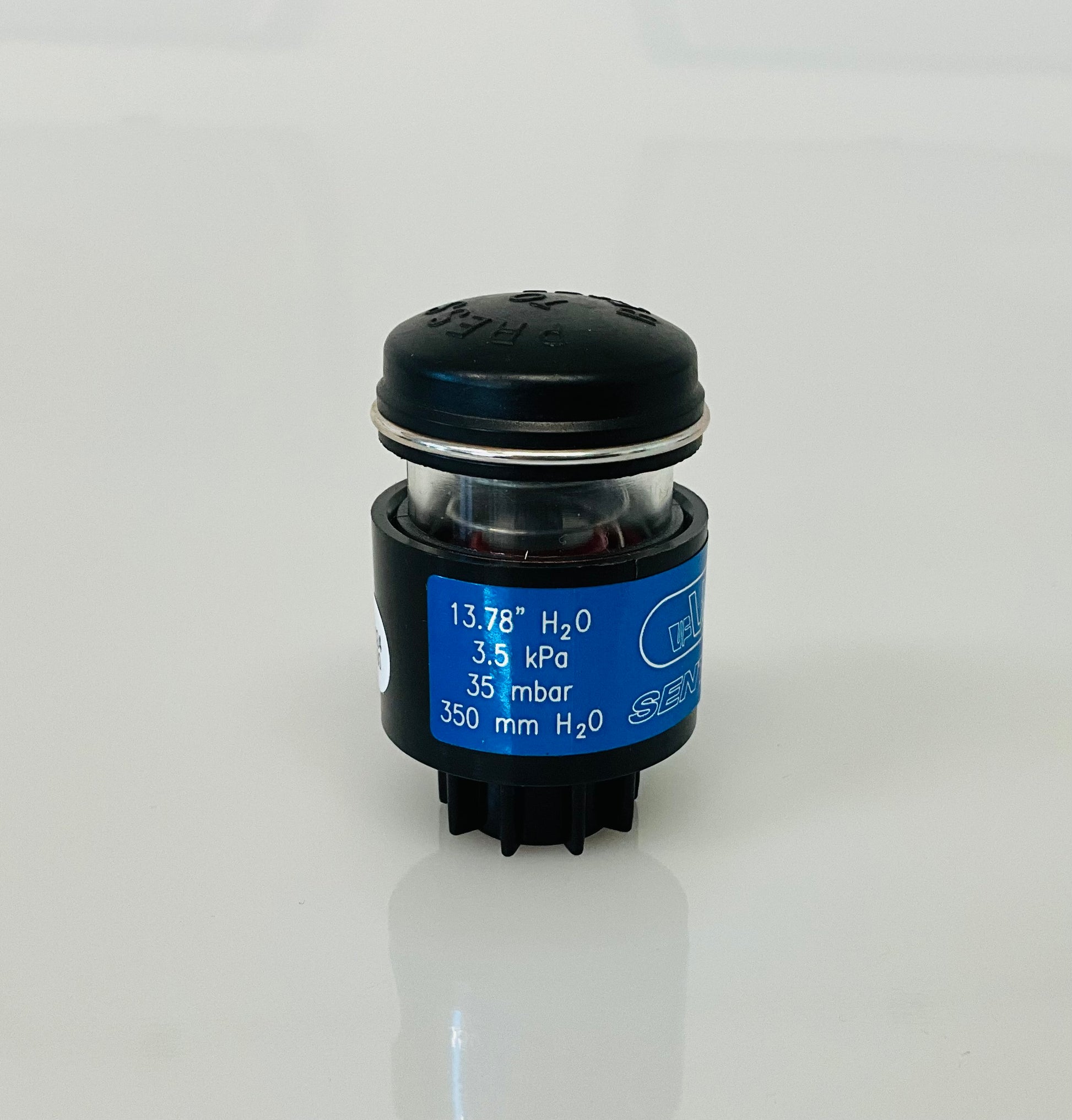 A small black cylindrical optical indicator with press button top, with a blue label reading '13.78" H2O, '3.5 kPa', '35 mbar', '350 mm H2O', photographed on a clean white background.