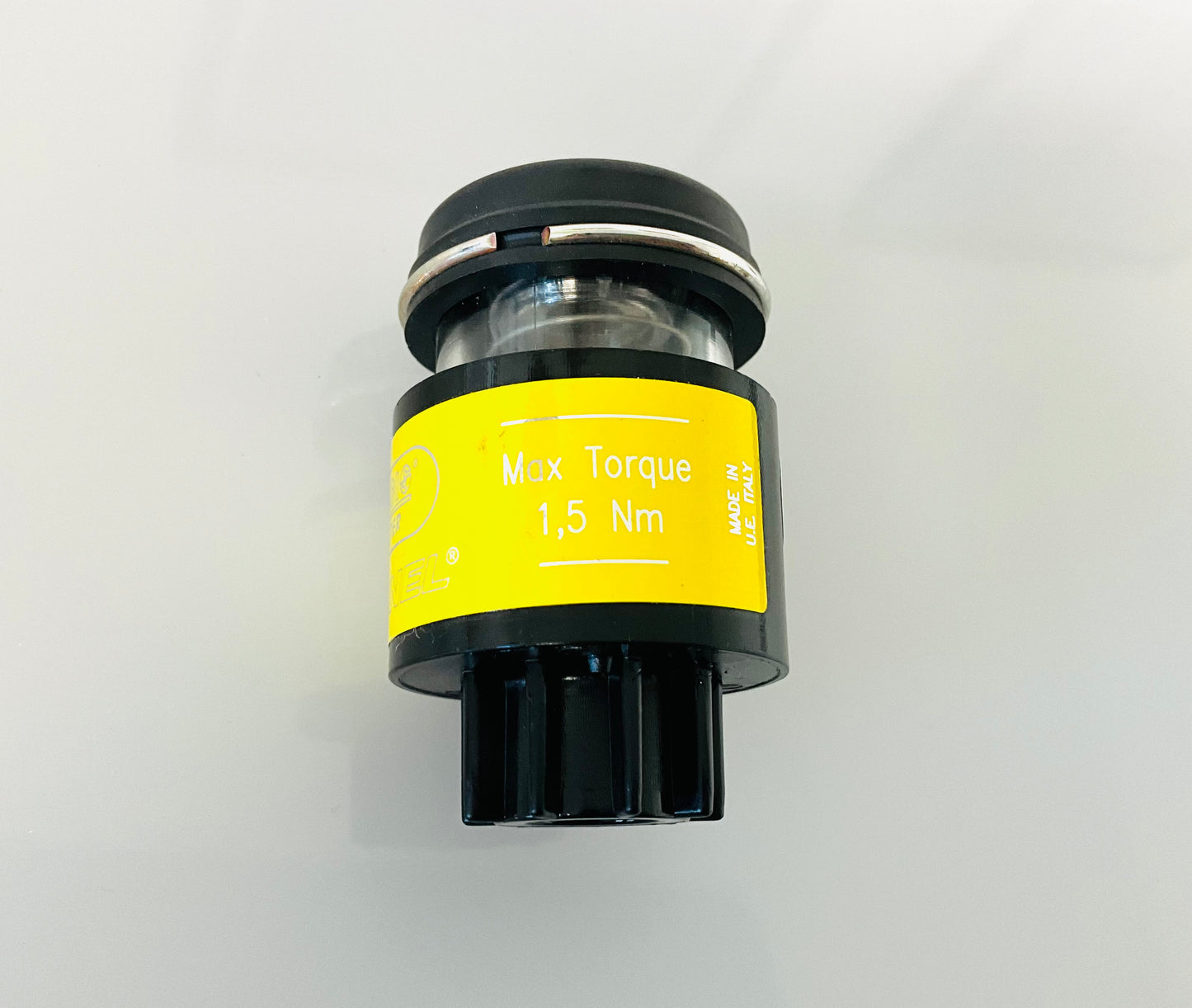 A small black cylindrical optical indicator with press button top, with a yellow label that reads 'Max Torque 1,5 Nm' and 'MADE IN U.E ITALY'. Shown on a reflective white surface.