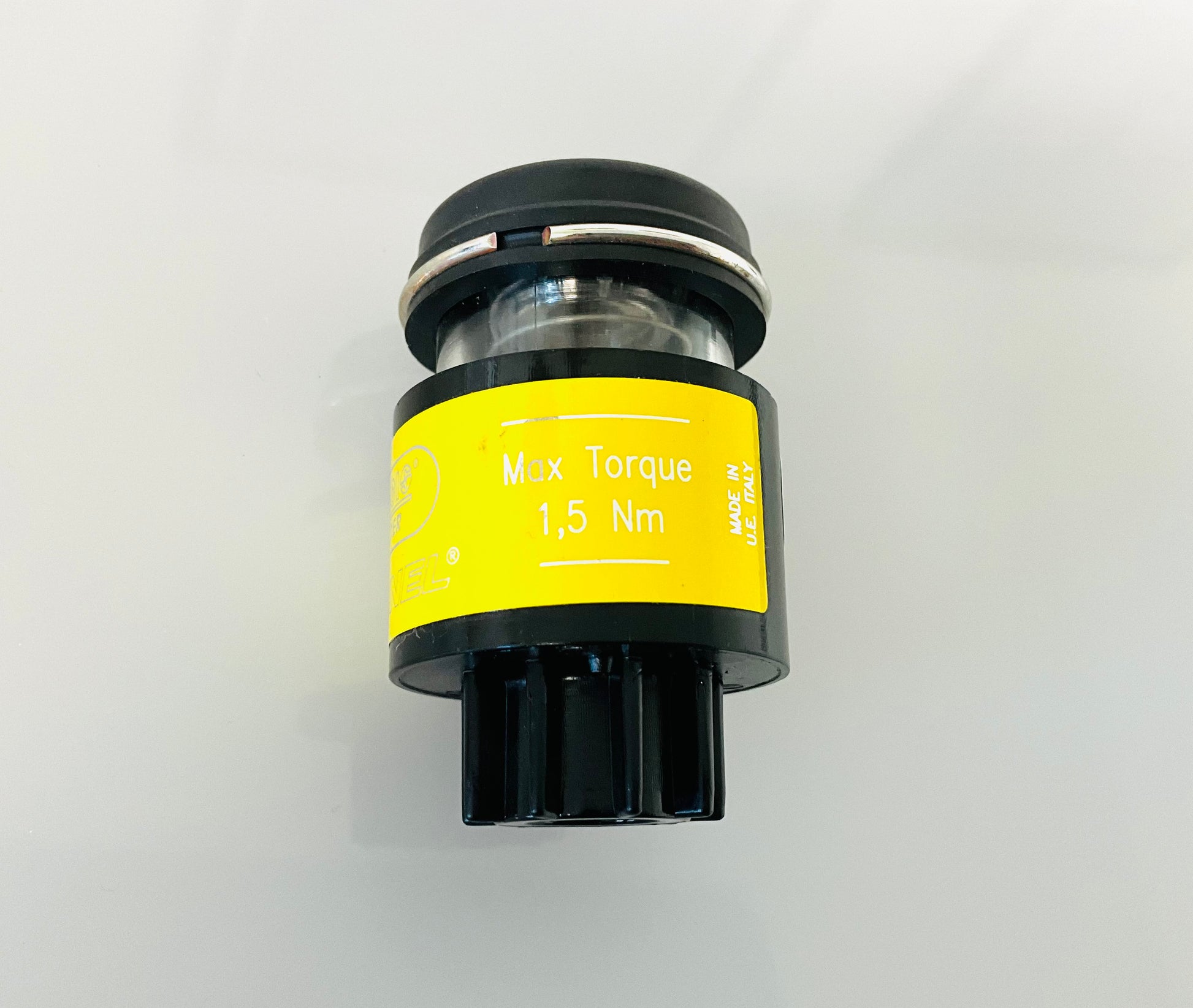 A small black cylindrical optical indicator with press button top, with a yellow label that reads 'Max Torque 1,5 Nm' and 'MADE IN U.E ITALY'. Shown on a reflective white surface.